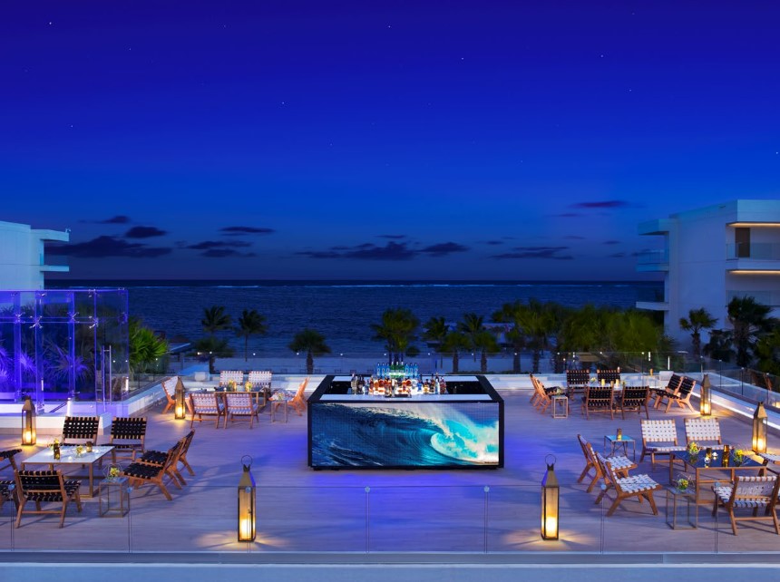 Outdoor terrace with lounge chairs and a bar, during sunset.