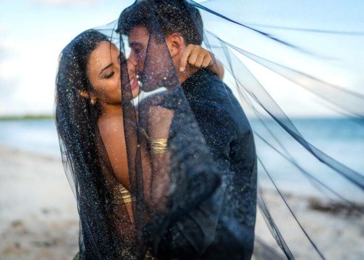 Elopement couple kissing on a beach under a veil
