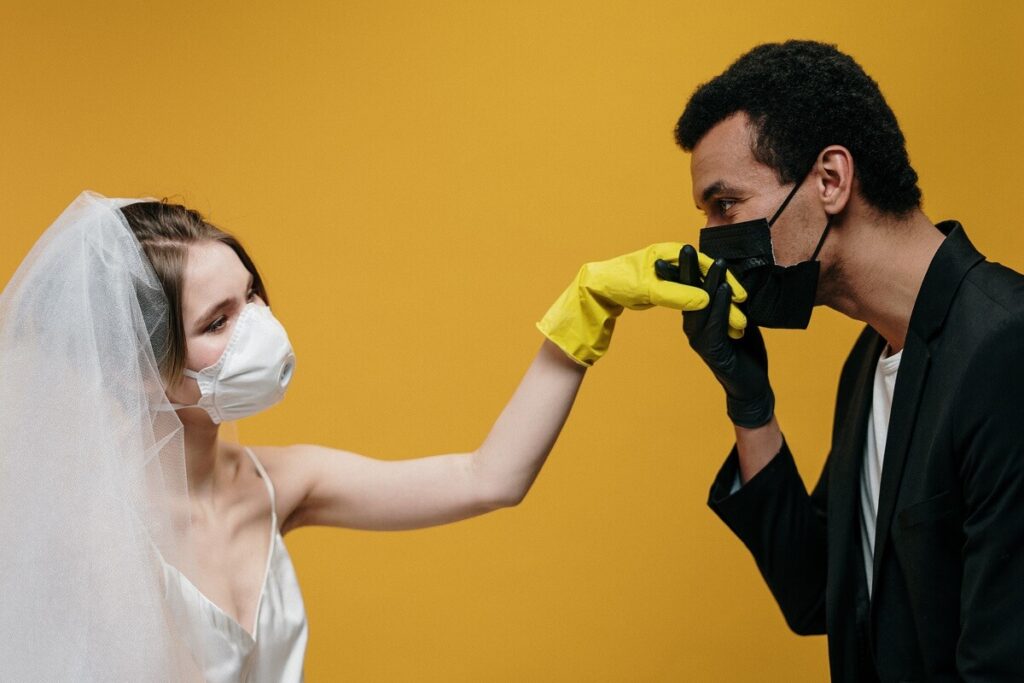groom with face mask kissing bride's hand