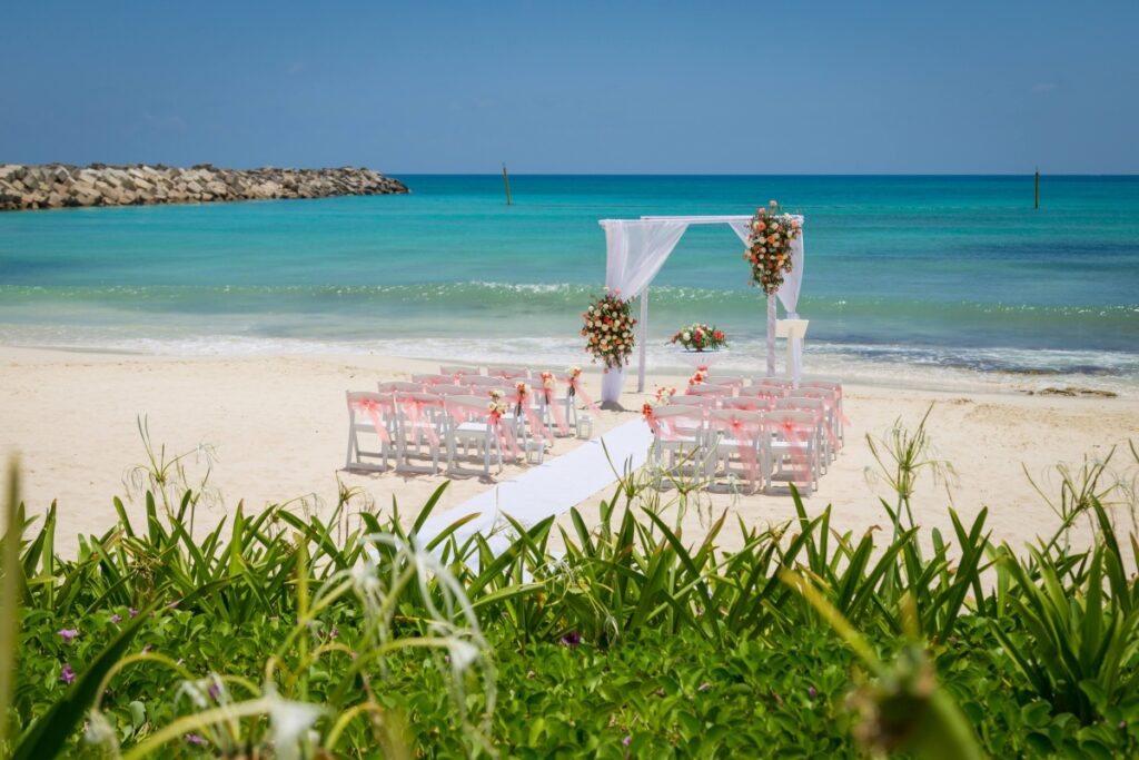 a beautiful wedding ceremony gazebo on the beach, with white and pink drapes and tropical flowers