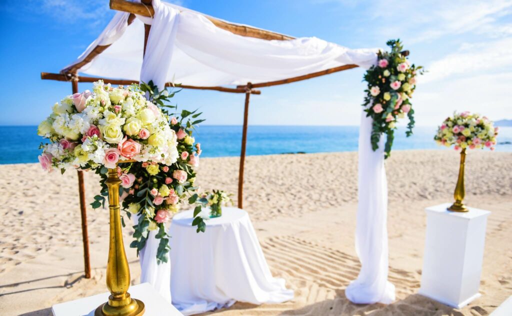 Beach destination wedding ceremony gazebo with white drapes and floral arrangements at Dreams Los Cabos
