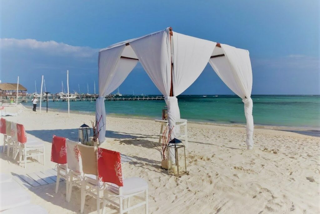 beach wedding ceremony set up with white drapes and coral chair covers