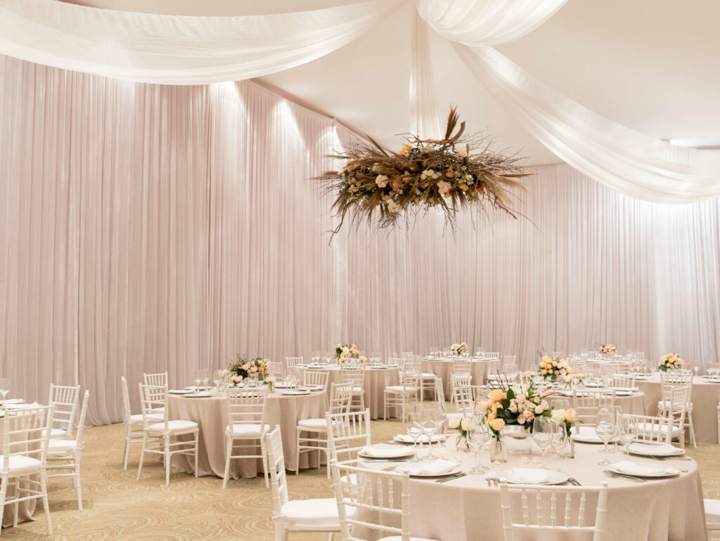 Ballroom set up for a wedding with white chairs and pink flowers