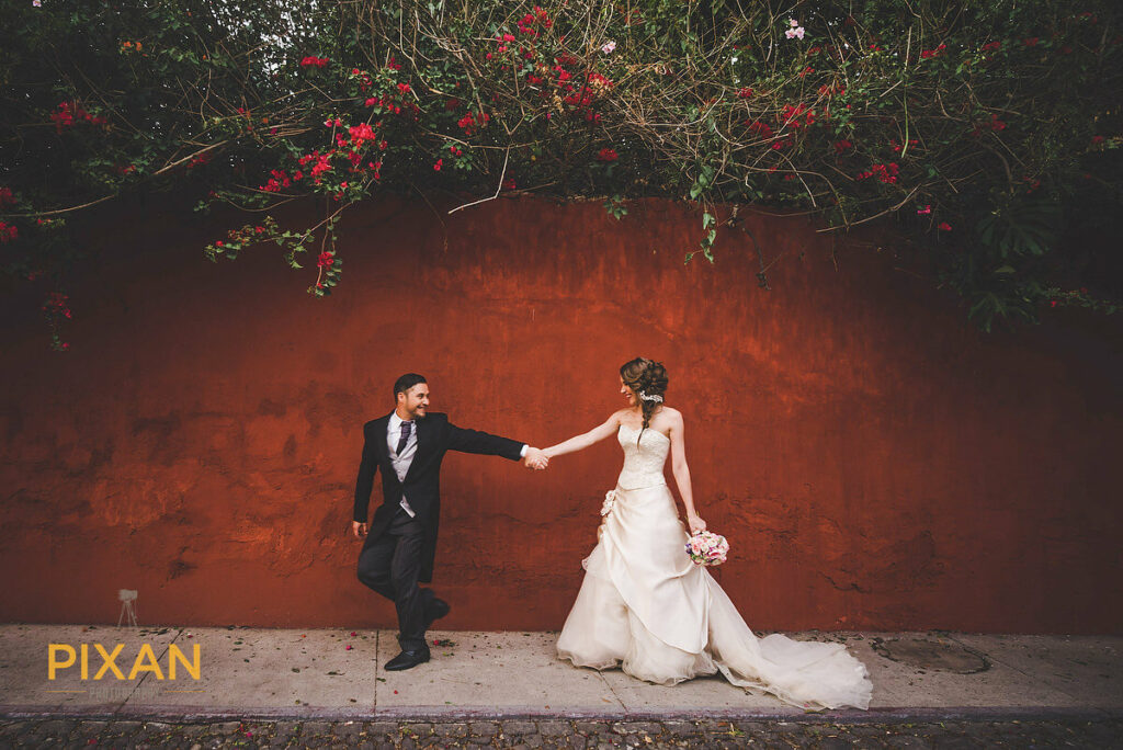 groom and bride holding hands in front of a runt colored wall