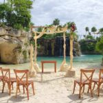 Destination Wedding gazebo on the beach with white drapes with flowers and a few wooden chairs at hotel xcaret