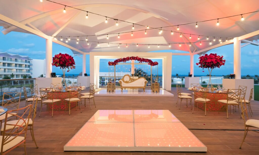 Wedding celebration all in white with red flowers and golden furniture with a dance floor in the middle