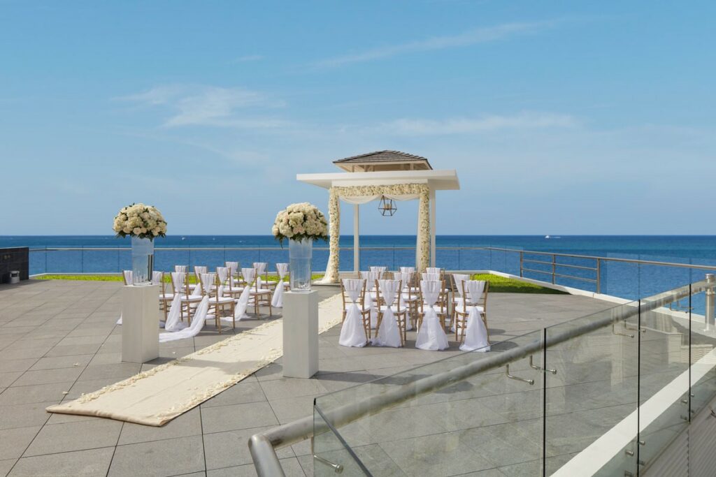 Sky wedding gazebo with ocean view decorated with white flowers, white drapes and two flower arrangemenets, in a resort in jamaica