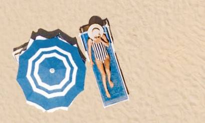 woman on beach lounger laying next to a parasol