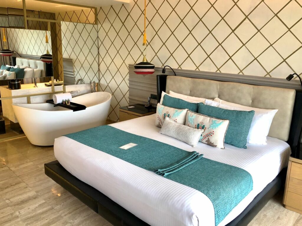 Hotel room with wooden furniture, blue fabrics, big mirrors and a bathtub