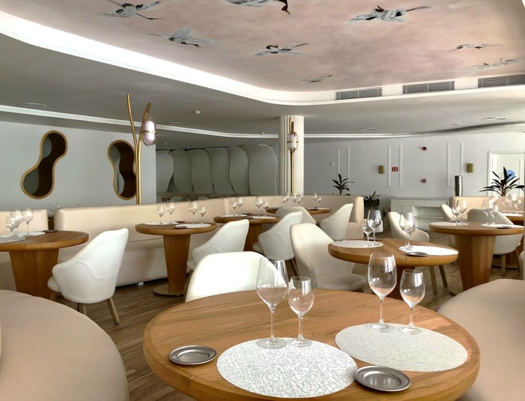 Resort restaurant decorated with wooden furniture, leather chairs and birds painted in the ceiling